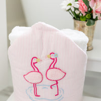 Pink hooded towel with flamingo design on a white surface with flowers in the background, 3 Marthas