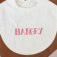 White bib with "HANGRY" emboidered against a wooden table