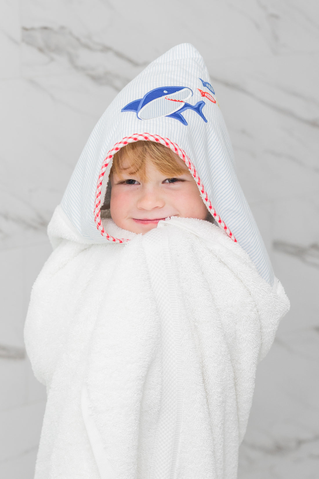Child wearing a white hooded towel with a blue shark design on a marble background, 3 Marthas