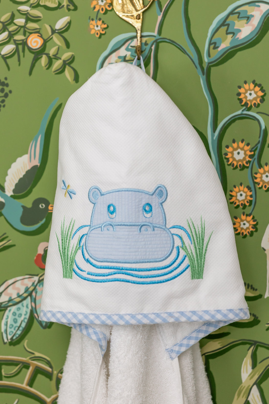 White hooded towel with blue hippo design hanging against a colorful floral and nature-themed background, 3 Marthas