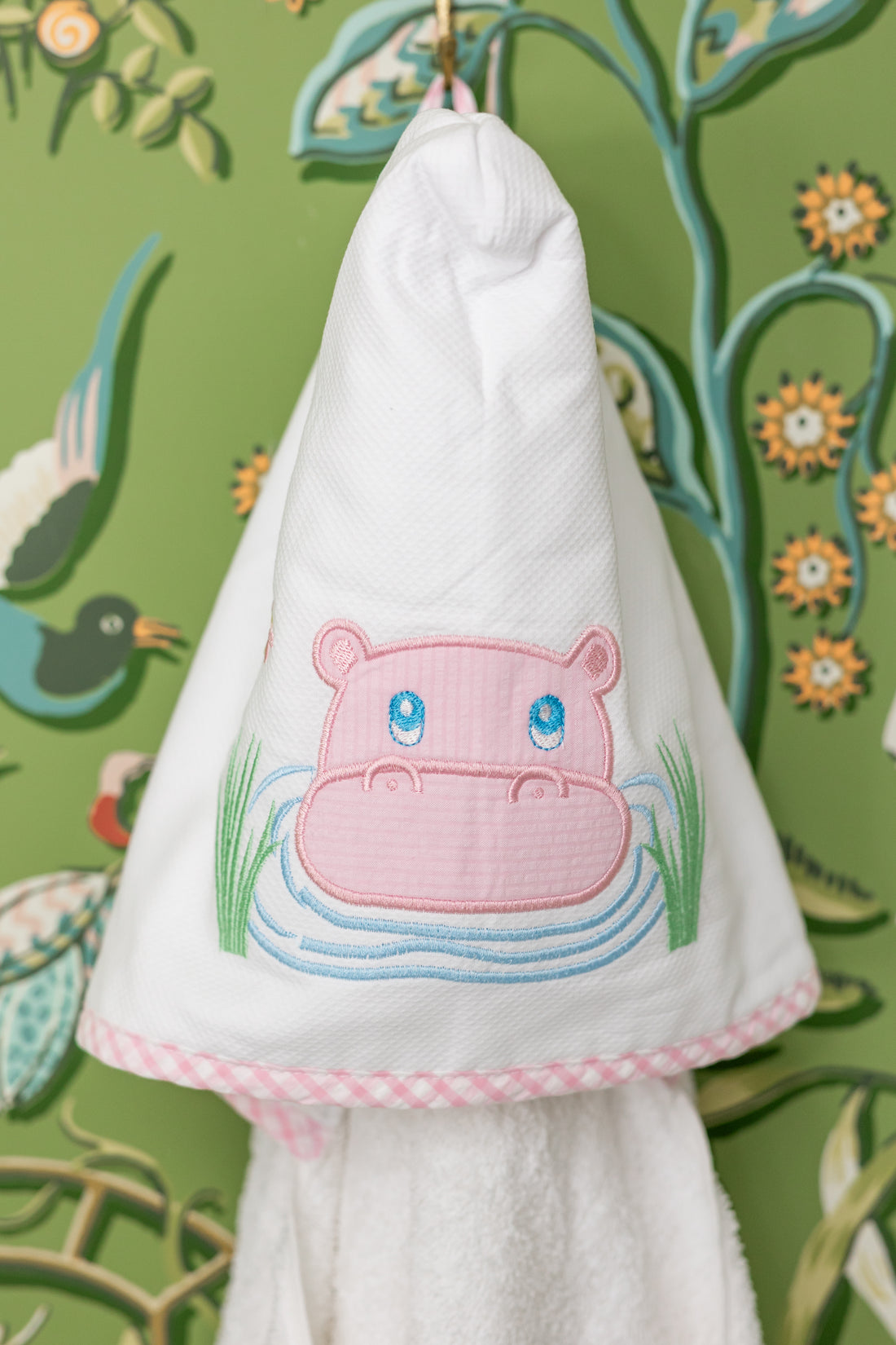 White hooded towel with pink hippo design hanging against a decorative green background, 3 Marthas