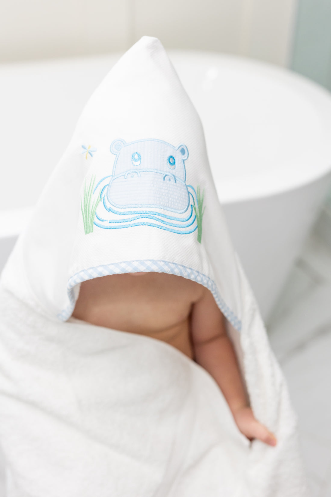 Child wrapped in hooded towel featuring a blue hippo applique sitting by the tub, 3 Marthas