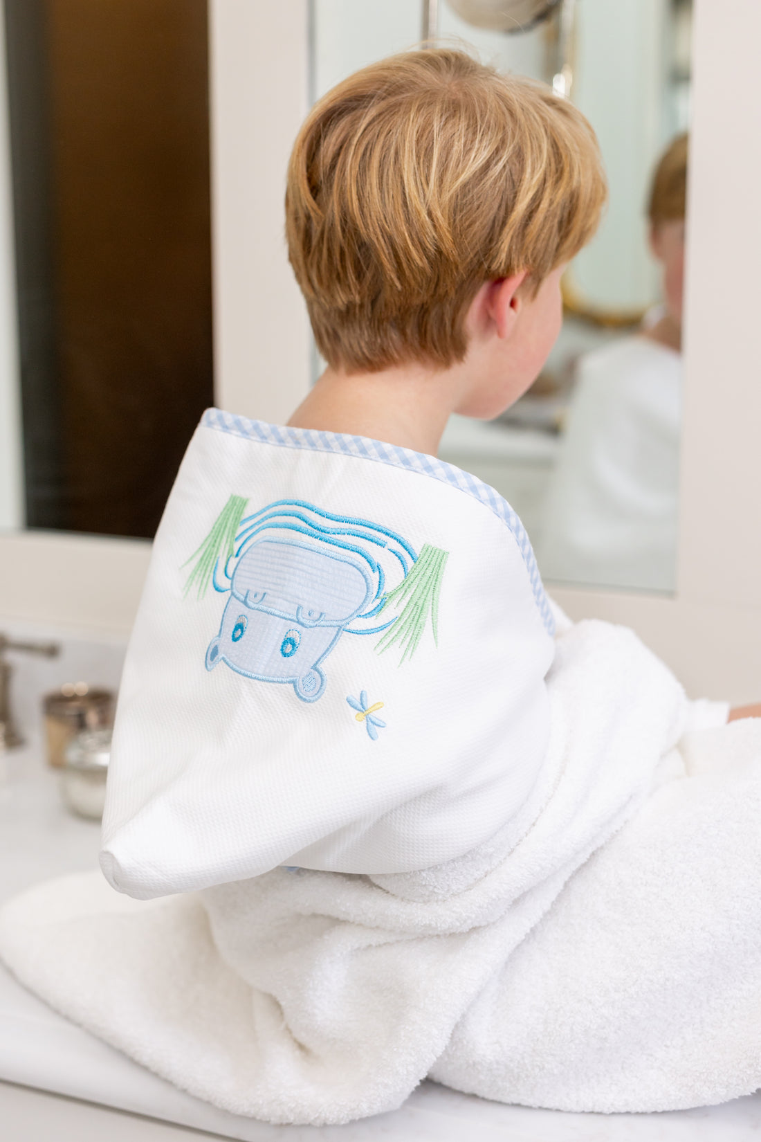 Child wrapped in hooded towel featuring a blue hippo applique sitting on bathroom counter, 3 Marthas