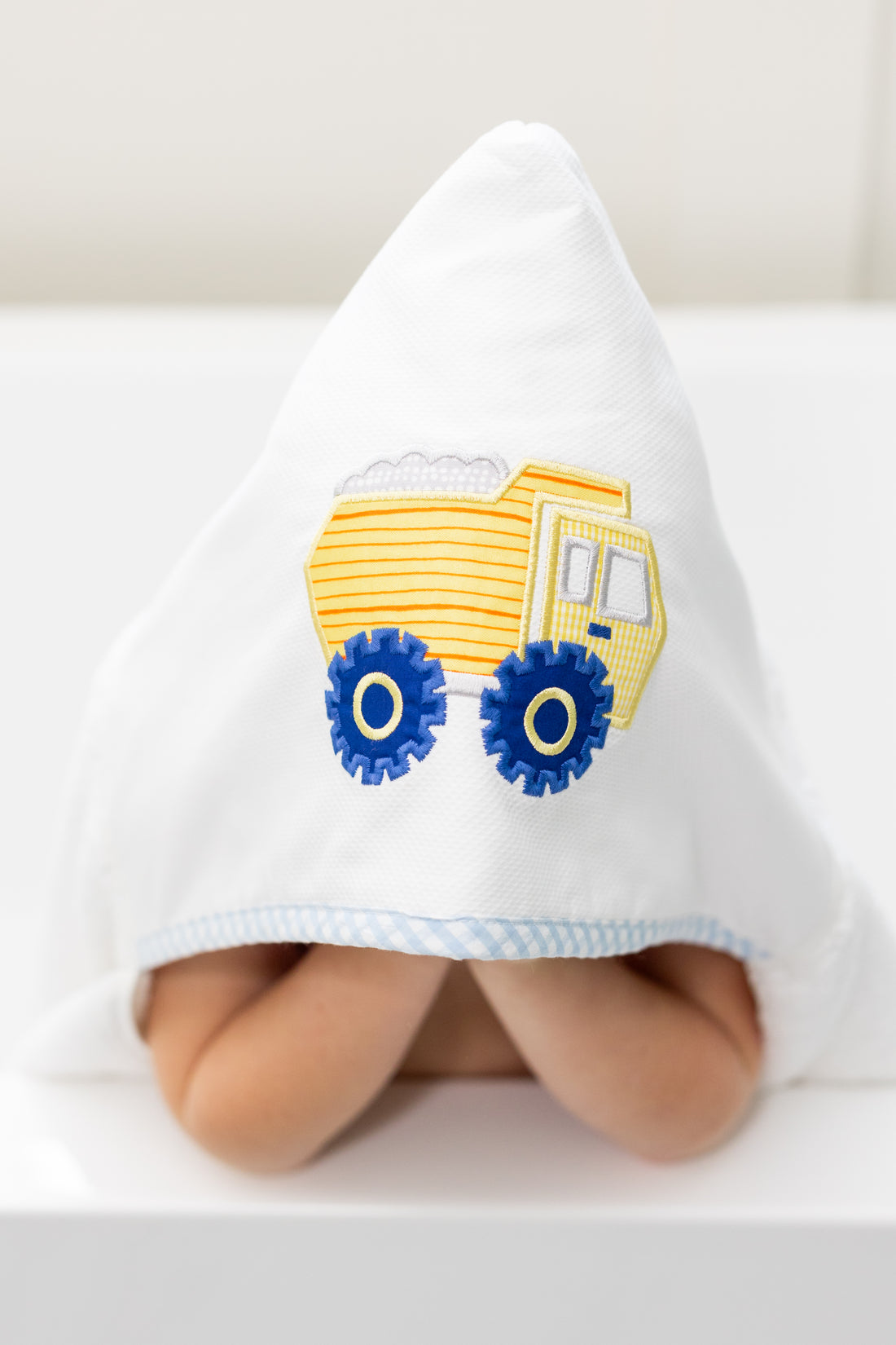 Child wearing a white hooded towel with a yellow dump truck design on a white background, 3 Marthas