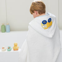 Child wrapped in a white hooded towel with a yellow dump truck, sitting on a bathtub with colorful rubber ducks, 3 Marthas