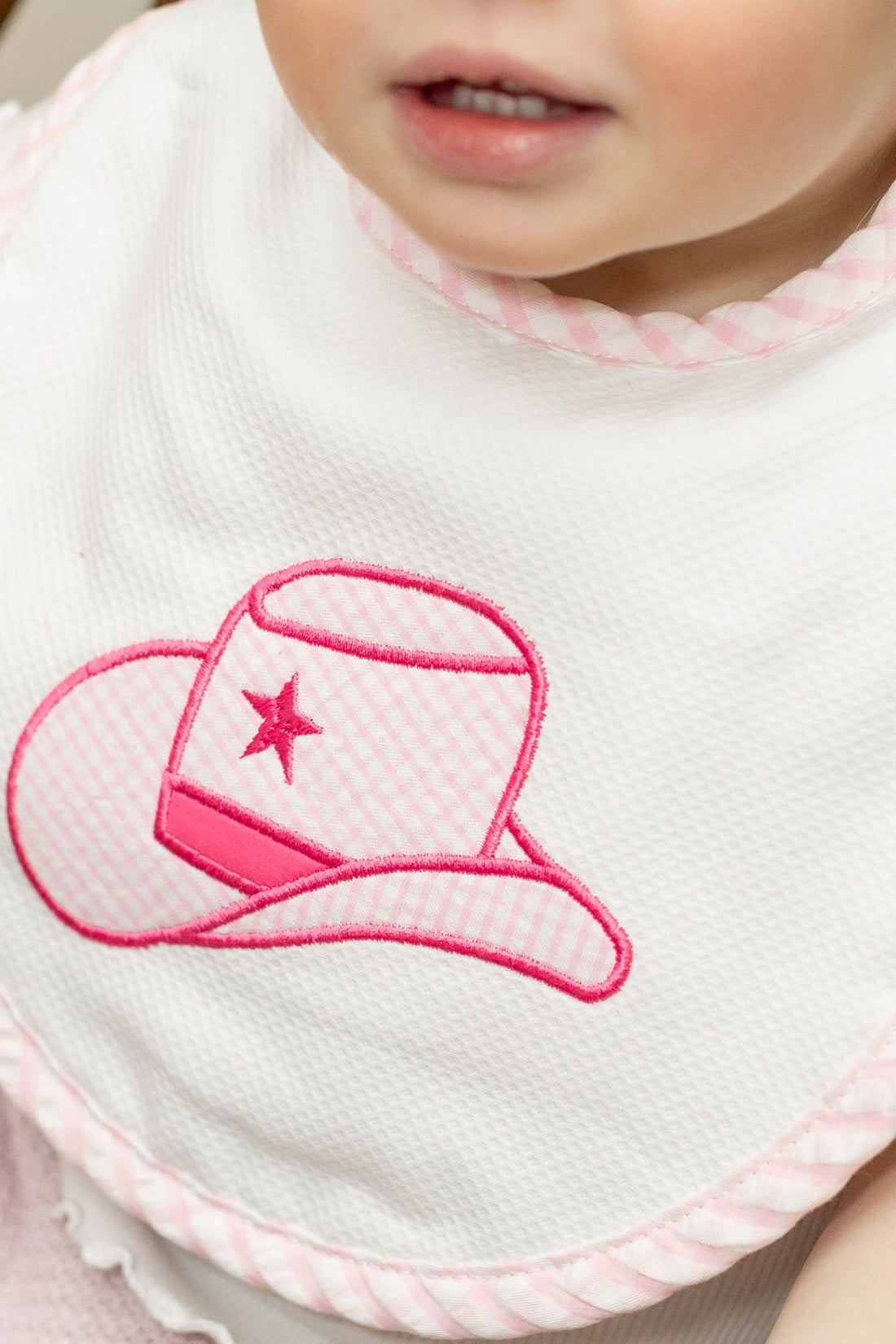 Baby bib with pink cowgirl hat design on a white background