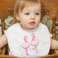 Child wearing a bib with flamingo design sitting in a wooden high chair, 3 Marthas