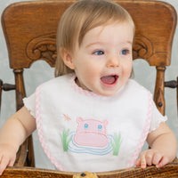 Baby wearing a bib with a pink hippo design, sitting in a wooden high chair, 3 Marthas