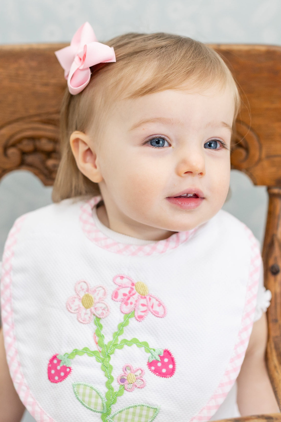 Baby sitting in a wooden chair wearing a bib with strawberry floral design, 3 Marthas