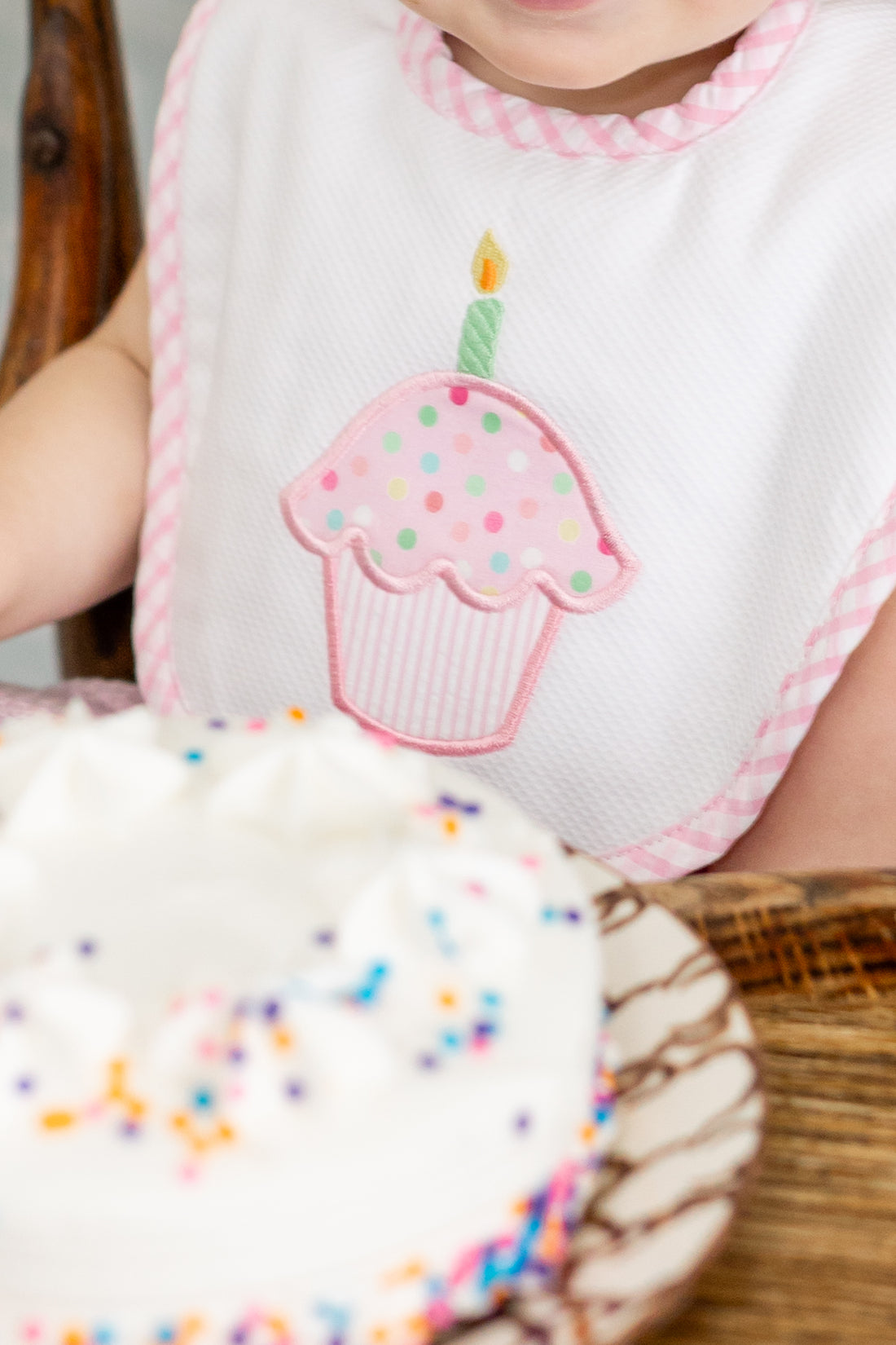 Child wearing a bib with a cupcake design, sitting next to a birthday cake, 3 Marthas