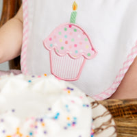 Child wearing a bib with a cupcake design, sitting next to a birthday cake, 3 Marthas