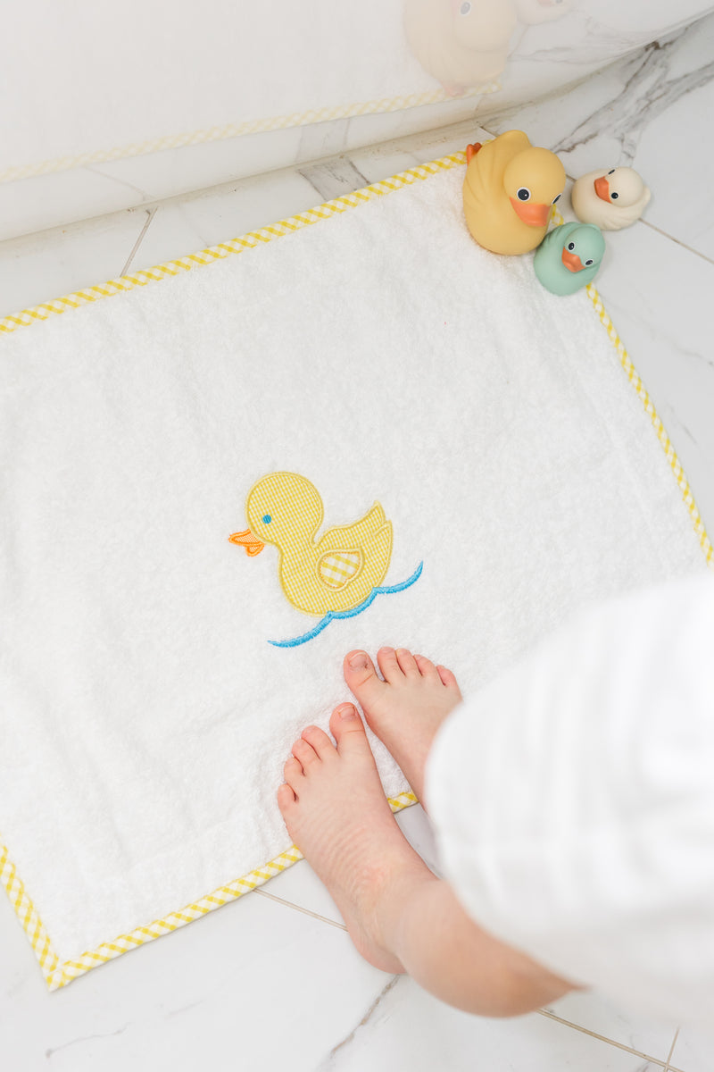 Baby's feet with bath toys on a bath mat featuring a yellow duck, 3 Marthas