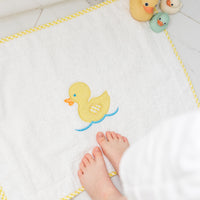 Baby's feet with bath toys on a bath mat featuring a yellow duck, 3 Marthas