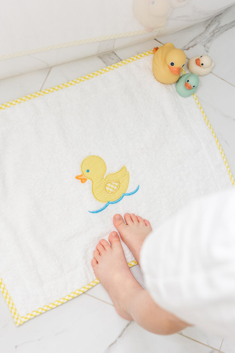 Baby's feet with bath toys on a bath mat featuring a yellow duck, 3 Marthas