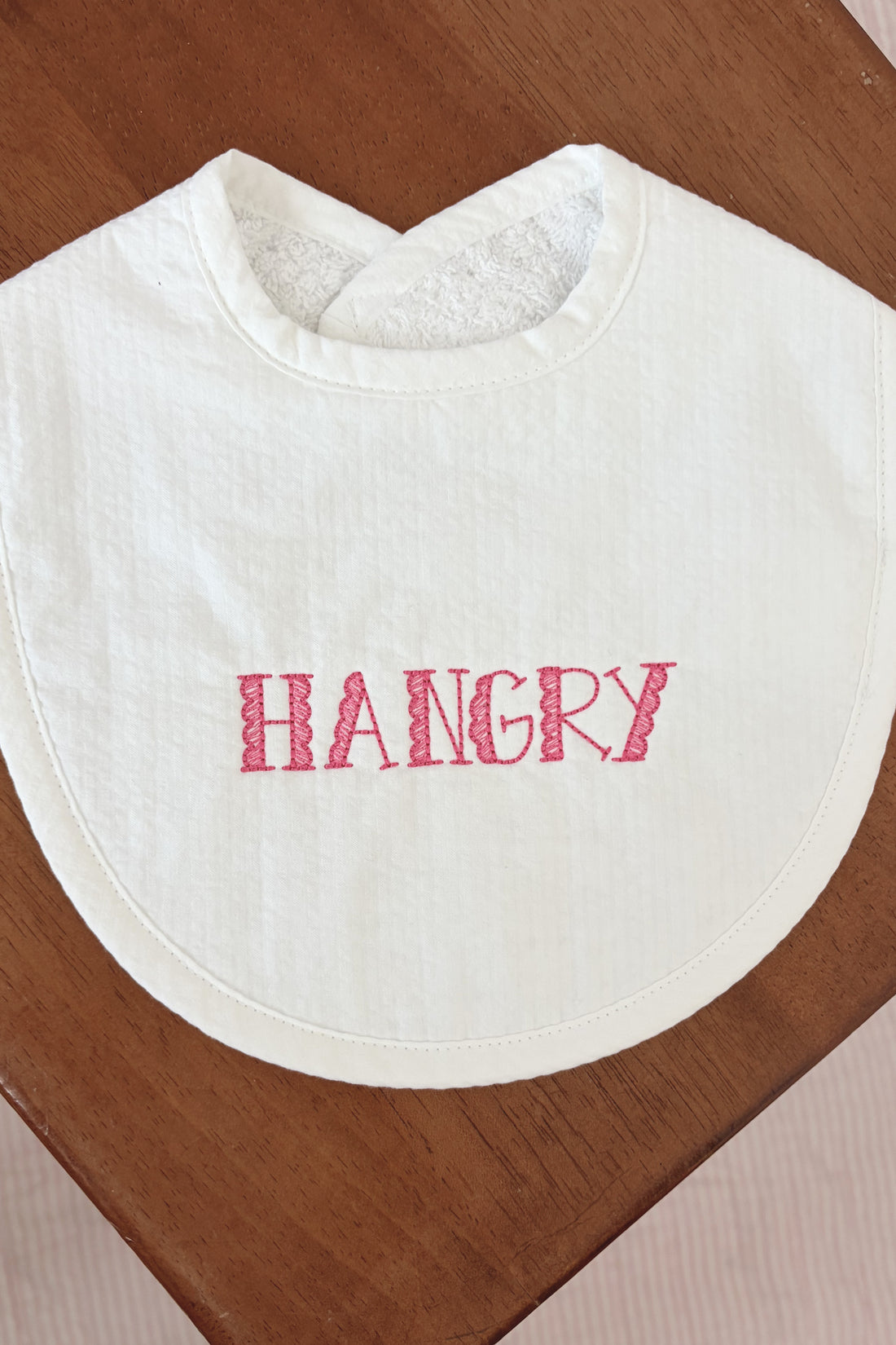 White bib with "HANGRY" emboidered against a wooden table