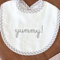 White bib with 'yummy!' embroidery on a wooden table